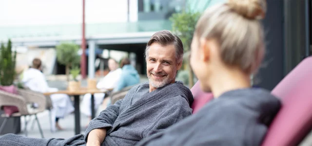 Ein Paar in Bademänteln im Aussenbereich lächeln sich an