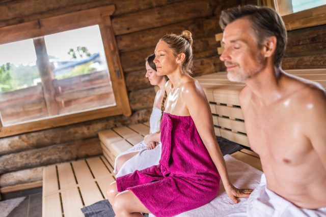 Zwei Frauen und ein Mann sitzen mit geschlossenes Augen in einer Sauna