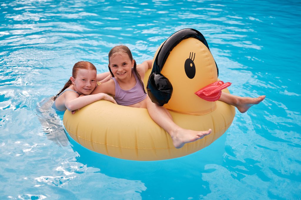 zwei Mädchen sitzen auf einer großen aufblasbaren Ente im Schwimmbecken