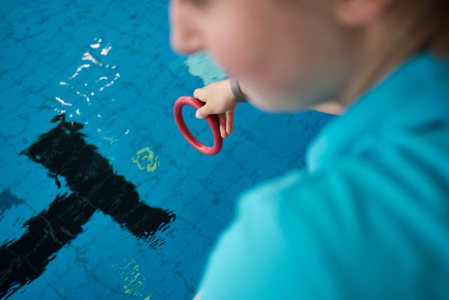 Rückansicht einer Person die einen Schwimmring in ein Schwimmbecken wirft